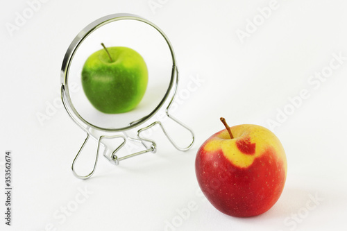 Red apple looking in the mirror and seeing itself as a green apple - Concept of daltonism and color blindness photo