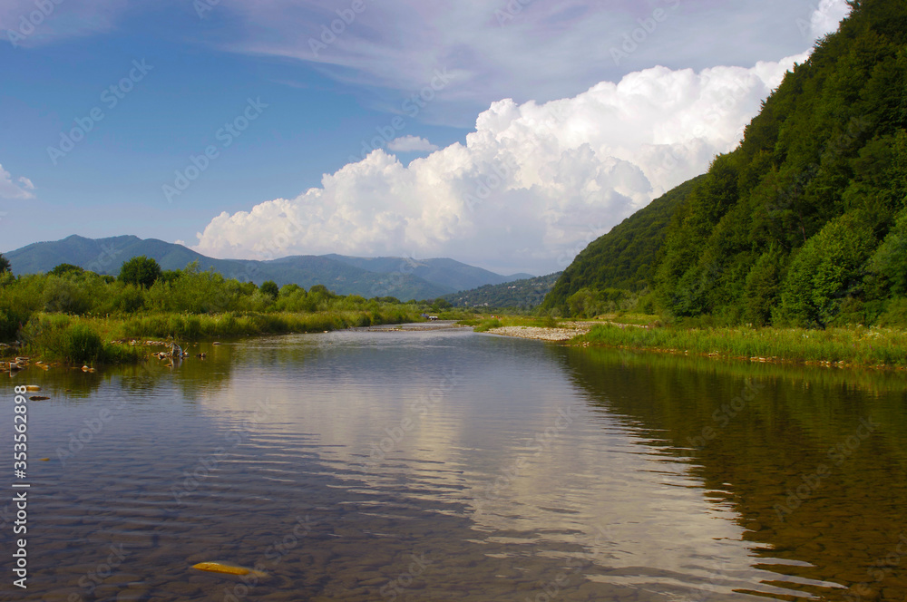 landscape with mountain river and cumulus clouds on a summer day before rain