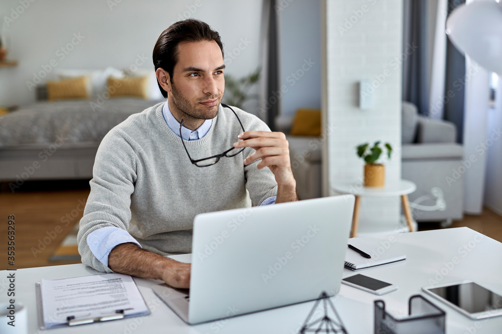 Fototapeta premium Smiling pensive entrepreneur working on laptop at home.