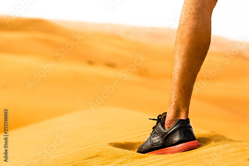 Photography Closeup crop of sporty runner man's leg and shoe standing alone in the desert sand dunes