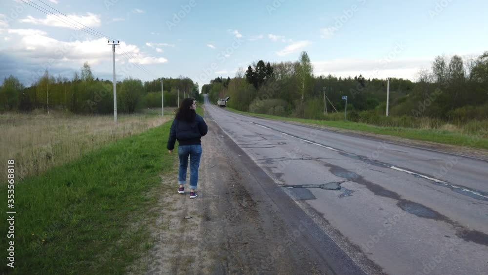 Girl walks along empty road and tries to catch car hitchhiking Girl walks along empty road and tries to catch car hitchhiking
