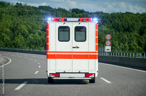Rear view of a single ambulance car on a highway with blue emergency lights