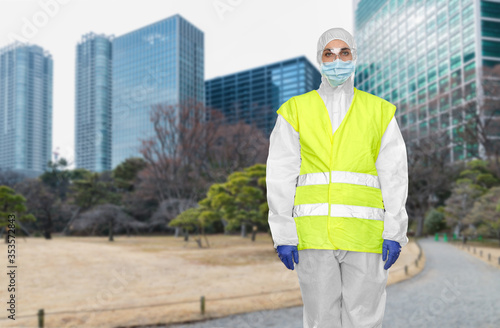 quarantine and pandemic concept - healthcare or sanitation worker in protective gear or hazmat suit, medical mask, gloves and goggles over tokyo city park background