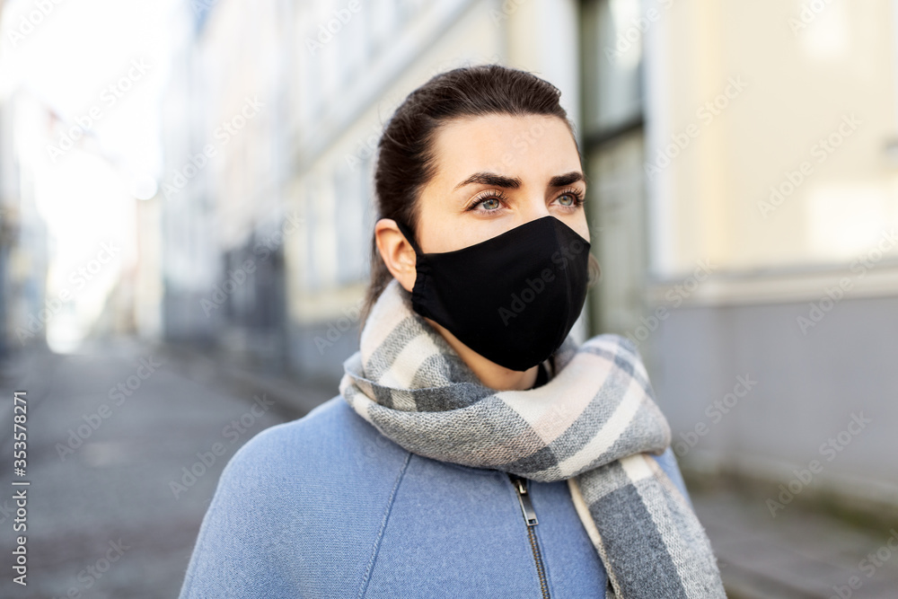 health, safety and pandemic concept - young woman wearing black face protective reusable barrier mask in city