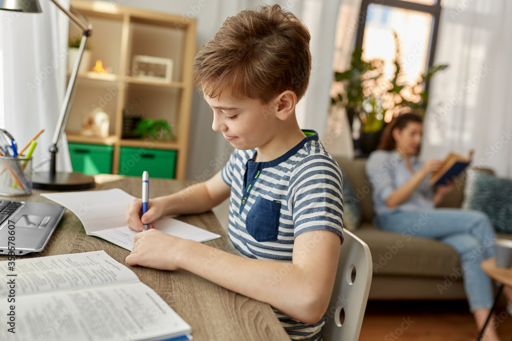 children, education and learning concept - happy student boy with book writing to notebook at home children, education and learning concept - happy student boy with book writing to notebook at home