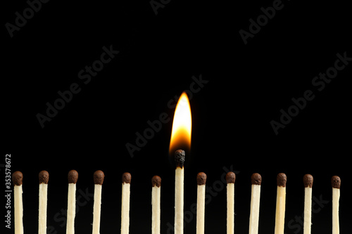 Burning match among unlit ones on black background, closeup