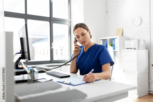 medicine, technology and healthcare concept - female doctor or nurse with computer and clipboard calling on phone at hospital photo