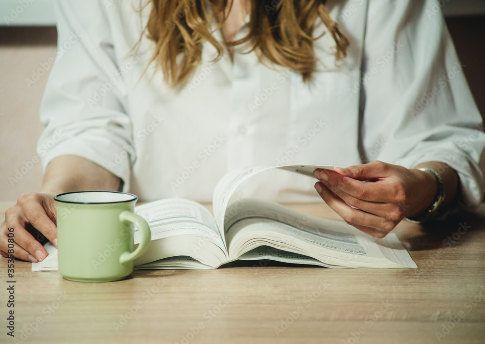 girl reading a book at the table and a cup with a coffee close-up girl reading a book at the table and a cup with a coffee close-up