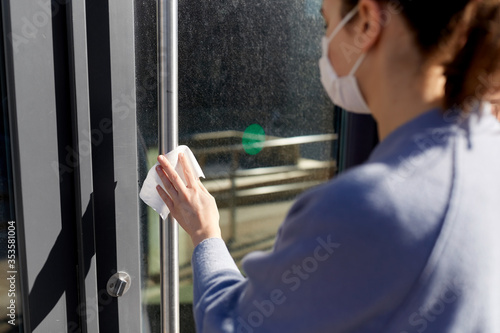 hygiene, health care and safety concept - close up of woman in mask cleaning outdoor door handle with antiseptic wet wipe