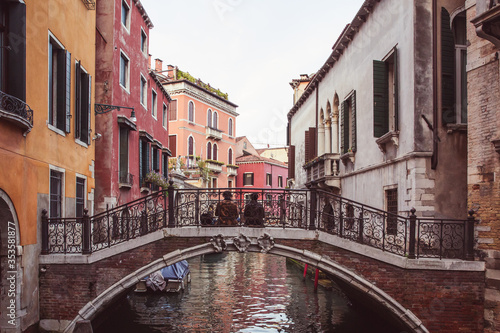 Two lovers sitting side by side on a bridge over a canal among pink buildings in Venice, Italy