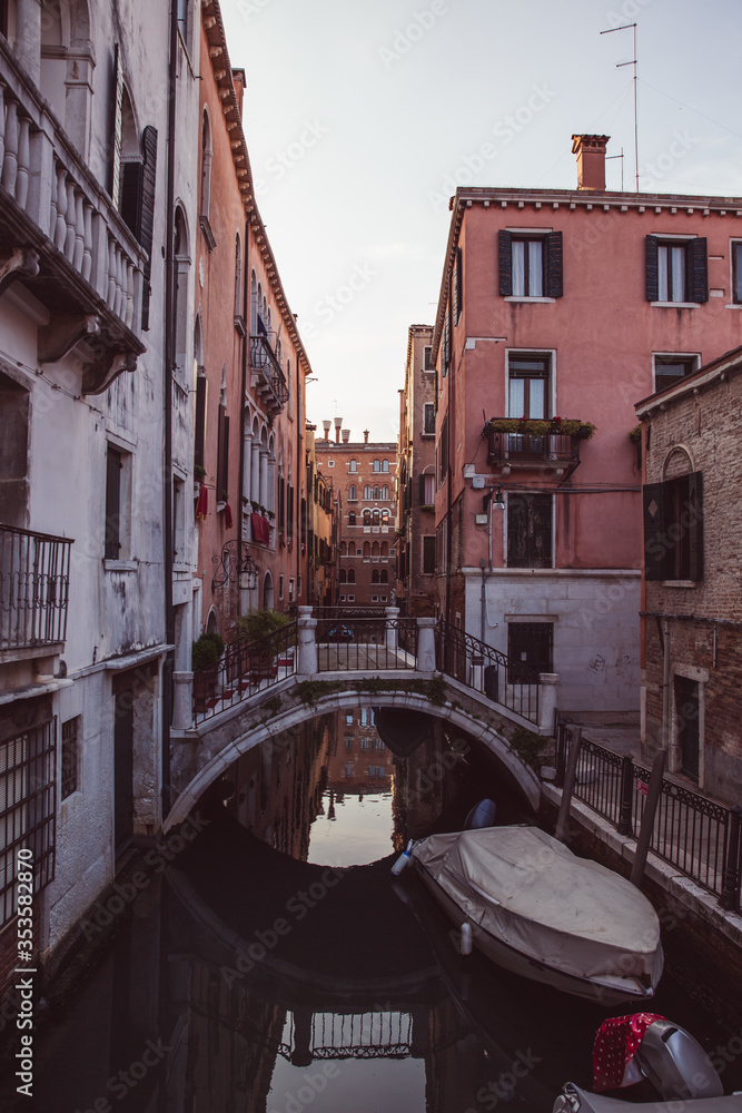 Empty streets and bridges of Venice, A small bridge and pink orange houses reflecting over a canal and a traditional moored gondola at sunset in Venice, Italy no people around. Lockdown, quarantine.