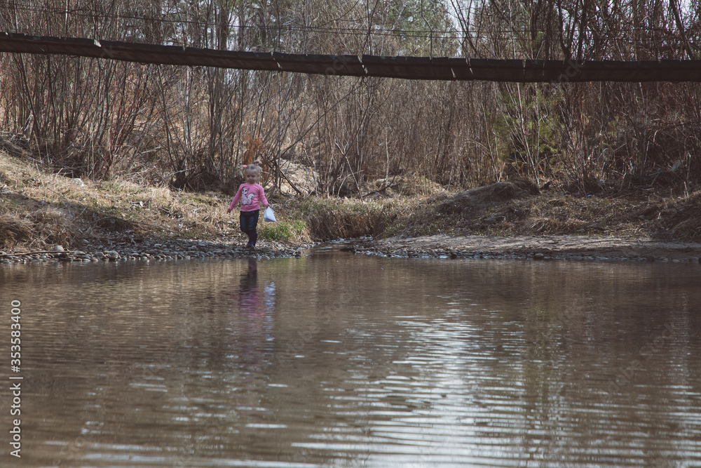Little girl in rubber boots launches paper white boats in creek in spring or autumn Little girl in rubber boots launches paper white boats in creek in spring or autumn