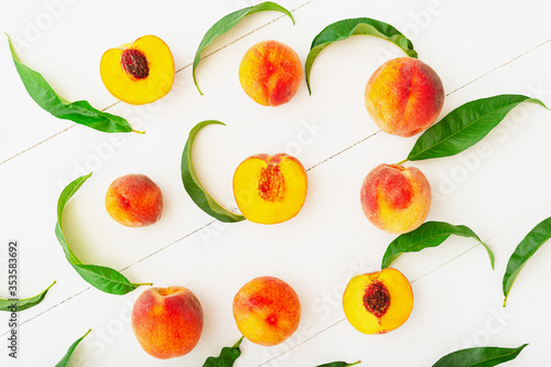 Fototapeta Naklejka Na Ścianę i Meble -  Peaches with leaves on white wooden background with peach in halves. Flat lay composition with ripe juicy peaches. Harvest of peaches for food or juice. Top view fresh organic peach fruit