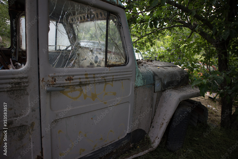 Closeup shot to an abandoned antique classic vintage pickup truck, with broken window and faded colour, under a tree, in Kozani, Macedonia, Greece.