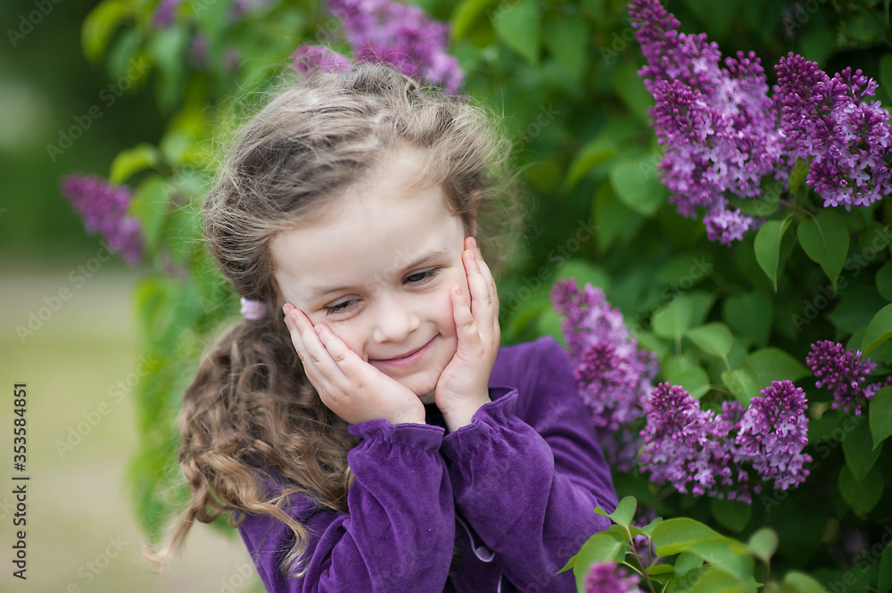 Cute toddler girl with loose curly hair among the bushes of lilac with bunches of flowers Cute toddler girl with loose curly hair among the bushes of lilac with bunches of flowers