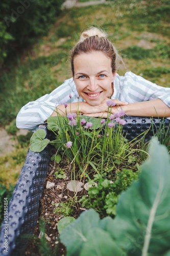 beautiful blond woman posing next to raised garden bed and her fresh vegetables