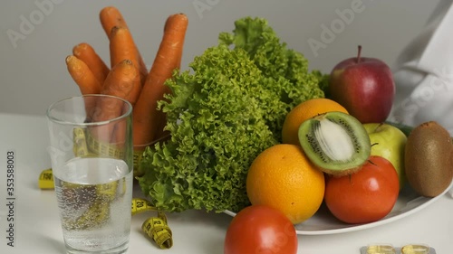 Vegetables and fruits on the table for a healthy diet. Diet. Lettuce, carrots, a glass of water, kiwi, tomato, orange and measuring tape photo