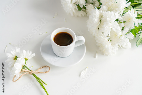 a coffee mug stands on a table on a white background, next to it are white chrysanthemums