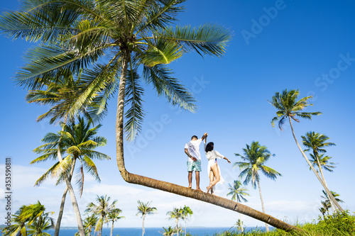 Obraz na płótnie A young couple is posing for a picture on a bent palm tree in Corregidor Island. Corregidor Island Siargao, also known as Casolian Island, is a dreamy tropical island in the south of the Philippines. w salonie