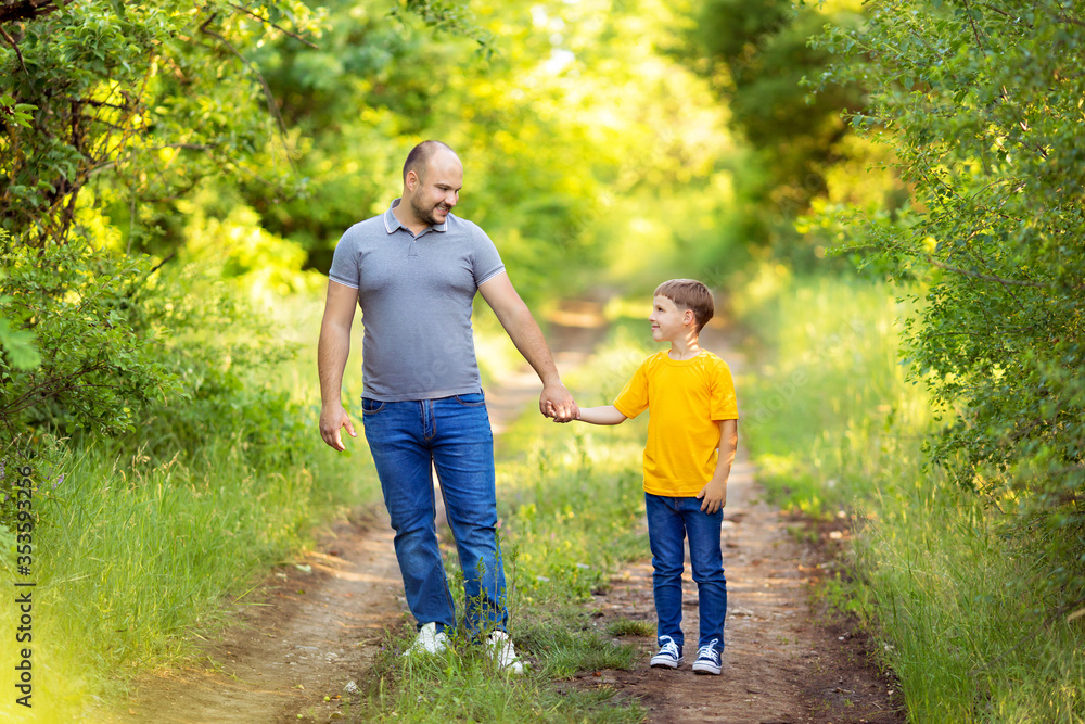 Happy young family: dad with son in casual wear, walk holding hands outdoors on a summer evening
