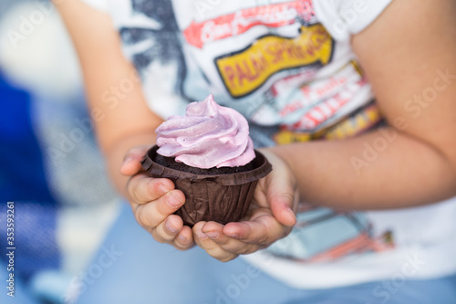  A child in jeans clothes holds in his hands a chocolate cupcake with blueberry cream.