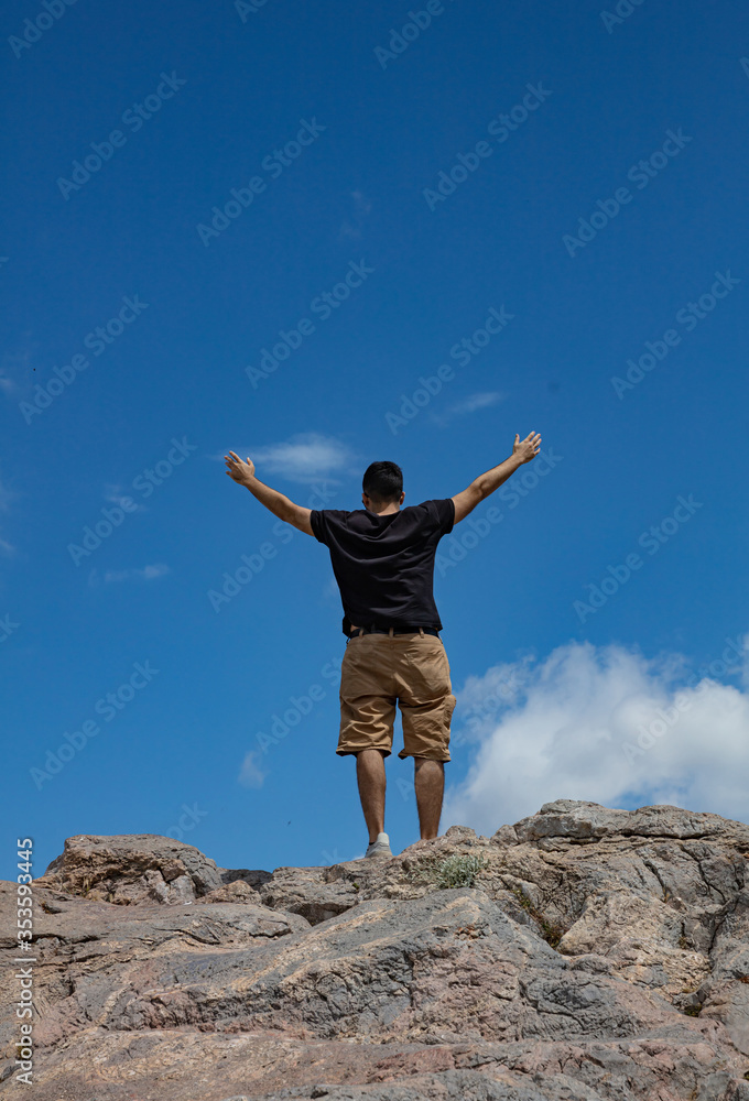 Young adult man back with raised arms on a mountain peak Young adult man back with raised arms on a mountain peak