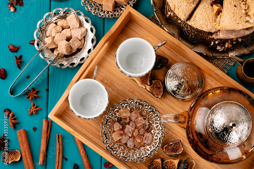 Two empty cups on a wooden tray with sugar cubes and turkish baklava on blue wooden table decorated with cinnamon sticks