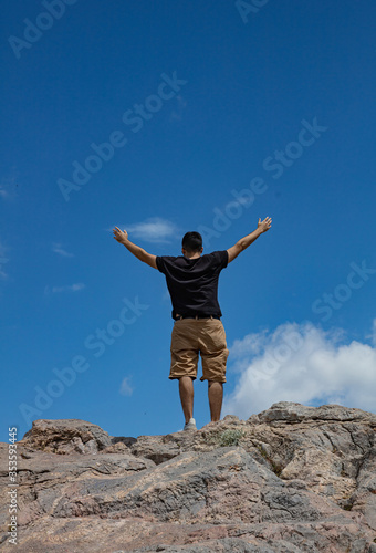 Young adult man back with raised arms on a mountain peak
