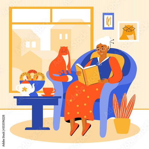 An elderly woman stays at home during the quarantine. Grandmother is sitting in a chair by the window, reading a book. Pensioner drinks tea with homemade cakes. Old woman spends time with her pet.