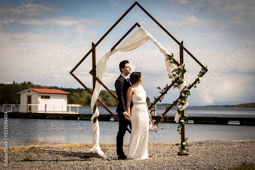A young couple is looking into the sun in front of a beautiful arch with an amazing lake view.