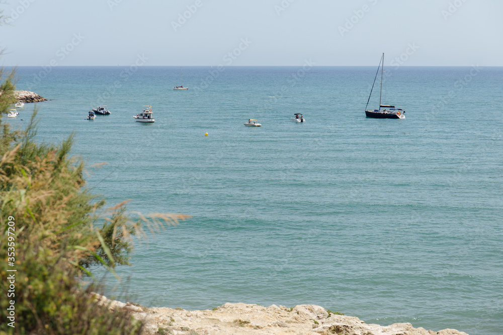 Selective focus of boats and yacht in sea and green plants on coast in Catalonia, Spain