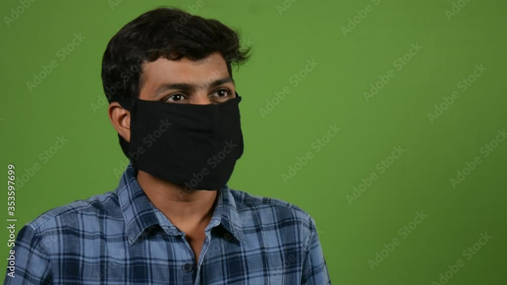 Portrait of a young man putting on a medical mask against air pollution during covid-19 pandemic on green screen Portrait of a young man putting on a medical mask against air pollution during covid-19 pandemic on green screen