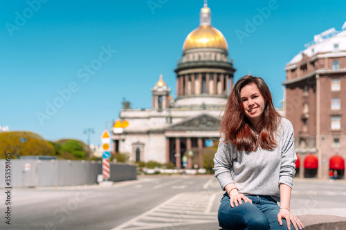 Portrait of a girl with long hair in a sweater on a Sunny summer day against the background of St. Petersburg street, with St. Isaac's Cathedral