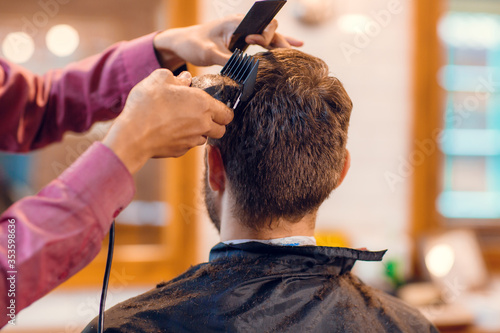 Young man getting hairstyling and haircutting in a barber shop or hair salon. Master wearing protective mask and cuts hair of men in the barbershop