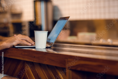 Close up of man's hands, coffee cup and laptop computer. Freelancer working from coffee shop