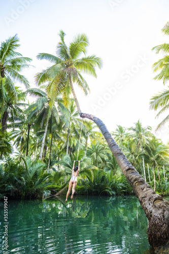 A beautiful girl wearing bikini is jumping from a coconut palm tre into the Maasin River in Siargao Island  Philippines. The Maasin River Palm Tree Swing is a tourist attraction in Siargao.