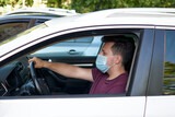 A man driving a car in a medical face mask during coronavirus outbreak, a taxi driver in a mask, protection from the virus. Quarantine, covid-19.