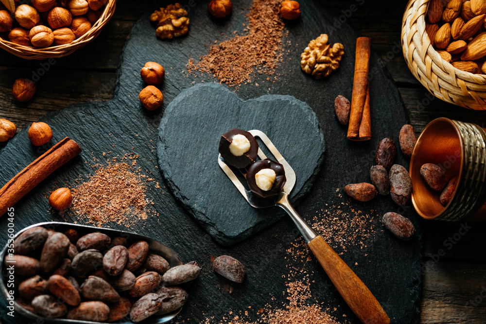 Cut handmade chocolate candies with haselnut on spatula on blackstone stand in heart shape. Chocolate candies with cocoa beans, cocoa powder around Cut handmade chocolate candies with haselnut on spatula on blackstone stand in heart shape. Chocolate candies with cocoa beans, cocoa powder around