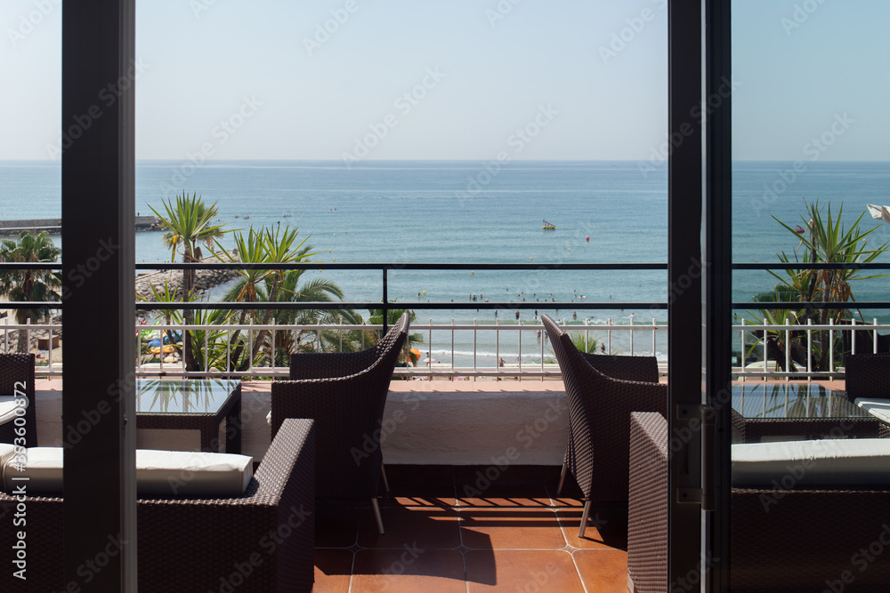 Chairs and tables on terrace with seascape and palm trees on coast in Catalonia, Spain