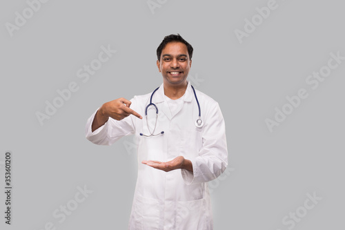 Doctor Pointing at Empty Open Hand in front of Chest Isolated. Indian Man Doctor Advertisment Concept