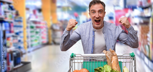 Euphoric supermarket customer with cart full of food in supermarket