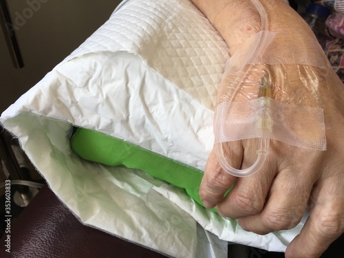 Obraz na płótnie Hand of an old patient being injected with intravenous fluid and drugs for operative care during chemotherapy at hospital