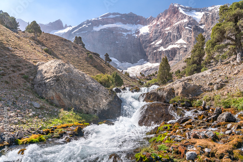 The beautiful mountain trekking road with clear blue sky and rocky hills and fresh mountain stream in Fann mountains in Tajikistan
