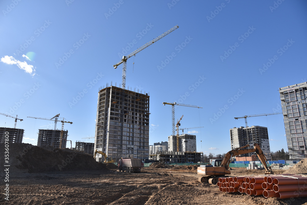 Tower cranes constructing residential buildings. Excavator on earthmoving at construction site. Backhoe dig ground for foundation and laying sewer pipes district heating. 
