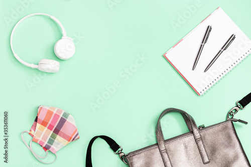 School bag and school supplies, notebooks, pens, white headphones mask for protection from infections on neo mint background with copy space. Top view.