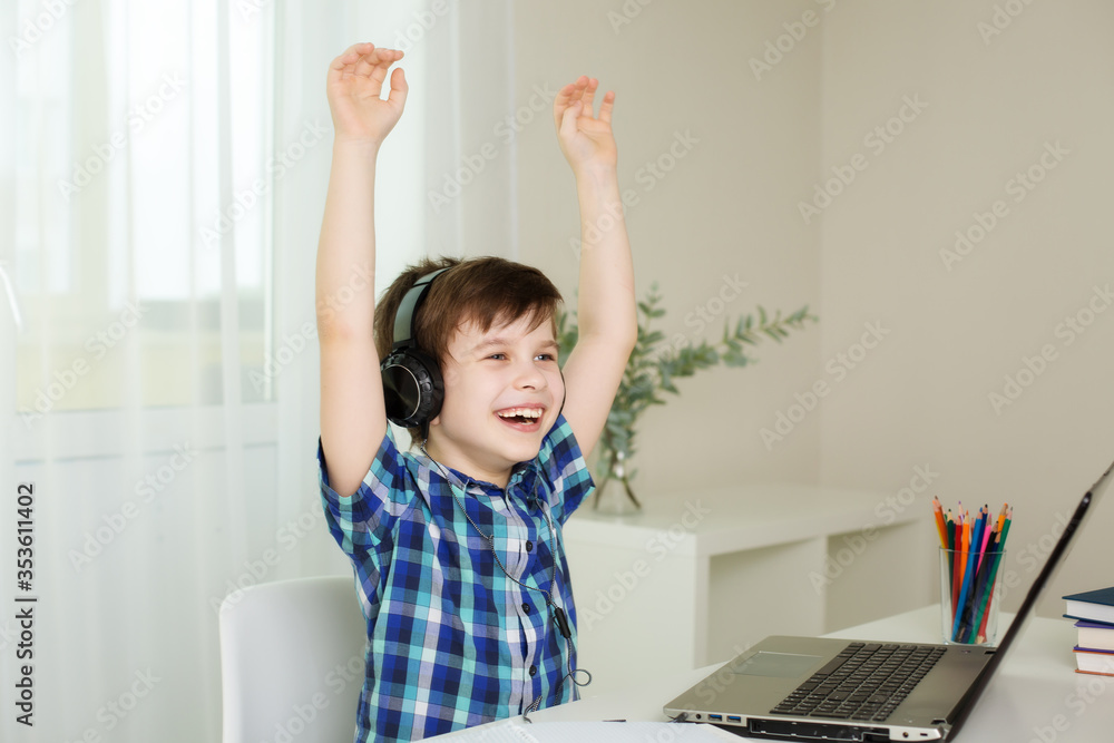 boy with headphones raised his hands and laughs, working on the computer at home boy with headphones raised his hands and laughs, working on the computer at home