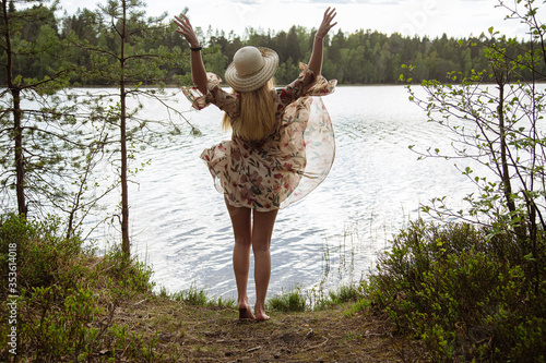 A girl in a beautiful dress on the shore of a forest lake.