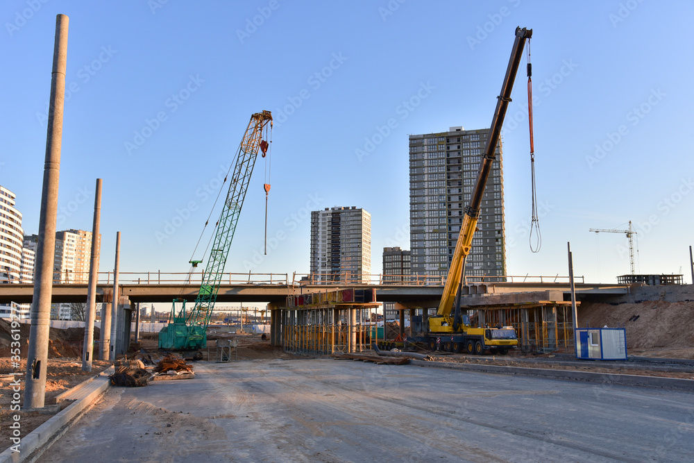 Work of truck crane and crawler crane on bridge project works. Roundabout traffic bridge construction and highway ramps. Road work on traffic highway, road intersection junction and freeway Work of truck crane and crawler crane on bridge project works. Roundabout traffic bridge construction and highway ramps. Road work on traffic highway, road intersection junction and freeway