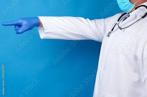 medic man in white coat with buttons, on hands wearing blue sterile gloves, showing hand gesture indicating the subject