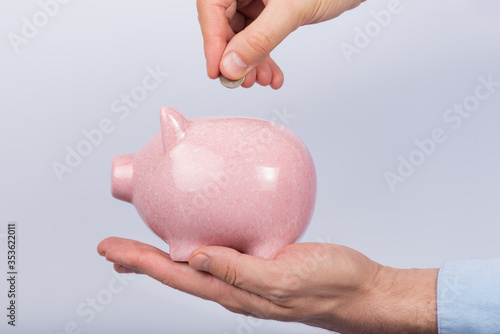Man holding piggy Bank and throws coins. White background. Savings concept. Side view